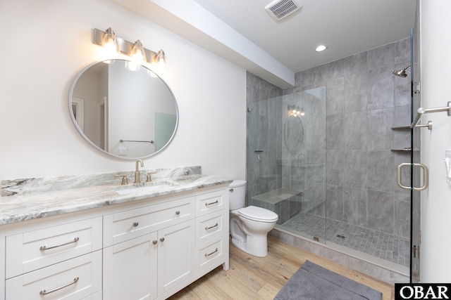 bathroom with visible vents, toilet, a stall shower, vanity, and wood finished floors