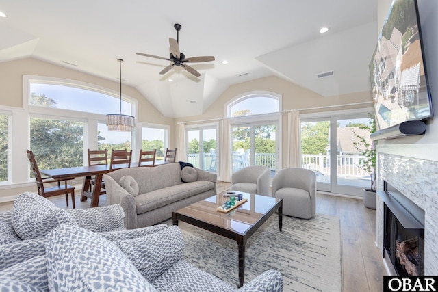 living room featuring light wood finished floors, visible vents, vaulted ceiling, a healthy amount of sunlight, and a fireplace