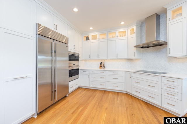 kitchen featuring wall chimney exhaust hood, built in refrigerator, black electric cooktop, light wood-type flooring, and white cabinetry