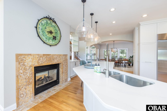 kitchen with white cabinets, hanging light fixtures, stainless steel built in refrigerator, light countertops, and light wood-type flooring