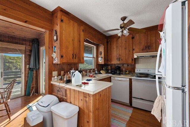 kitchen with under cabinet range hood, a peninsula, white appliances, light countertops, and brown cabinets