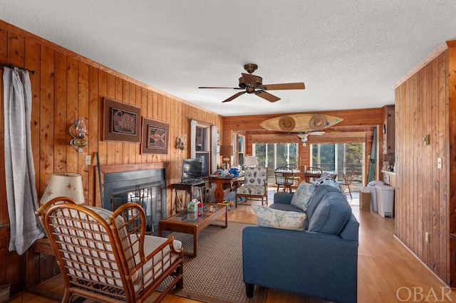 living area featuring a textured ceiling, light wood finished floors, wood walls, and a glass covered fireplace