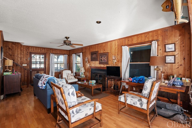 living area featuring ceiling fan, a textured ceiling, wood walls, wood finished floors, and a glass covered fireplace