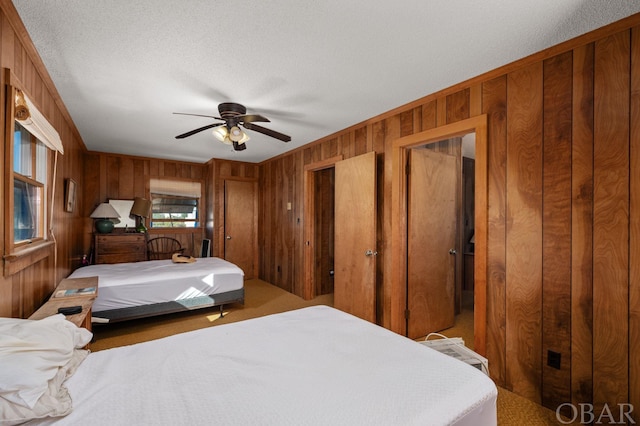 carpeted bedroom with wood walls, a textured ceiling, and ceiling fan