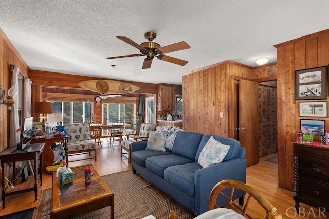 living area with ceiling fan, light wood finished floors, and wooden walls