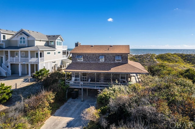 back of house with a carport, concrete driveway, a water view, and a chimney