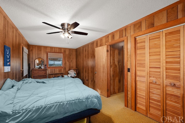 bedroom featuring a closet, a ceiling fan, light carpet, wooden walls, and a textured ceiling