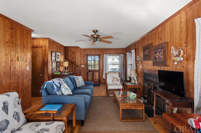 living area featuring a ceiling fan, wood walls, a textured ceiling, and wood finished floors