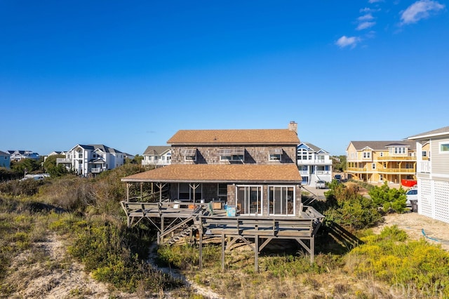 back of house featuring a sunroom, a chimney, a residential view, and a deck