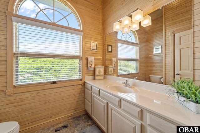 bathroom featuring wooden walls, vanity, toilet, and visible vents