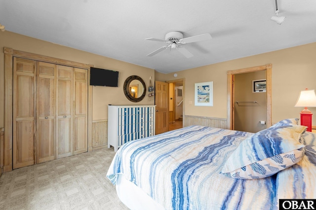 bedroom with a ceiling fan, wainscoting, and light carpet