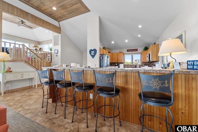 kitchen featuring vaulted ceiling, brown cabinetry, stainless steel appliances, and a breakfast bar area