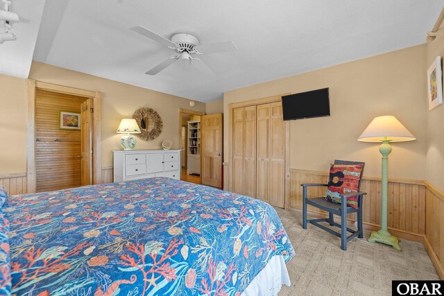 bedroom featuring a closet, wood walls, wainscoting, light carpet, and ceiling fan