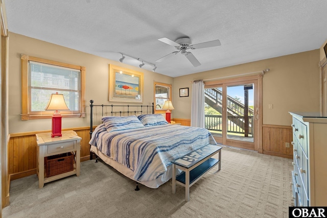 bedroom featuring wooden walls, a textured ceiling, rail lighting, access to exterior, and a wainscoted wall