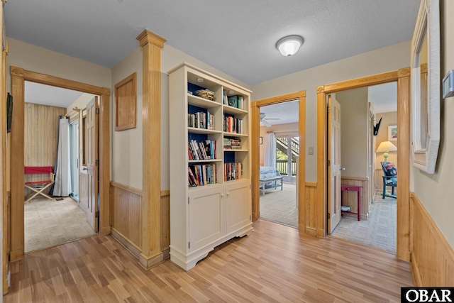 hall with light wood-style floors, a wainscoted wall, and wooden walls