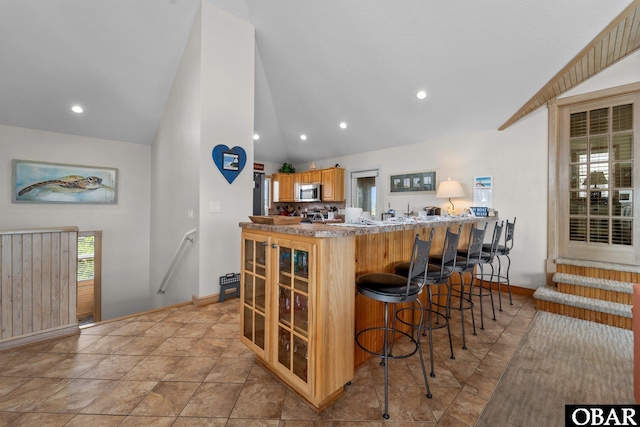 kitchen featuring a peninsula, a breakfast bar, baseboards, stainless steel microwave, and vaulted ceiling