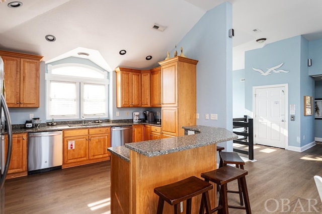 kitchen featuring dark wood finished floors, stainless steel dishwasher, a kitchen bar, and visible vents