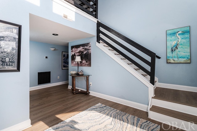 stairs with visible vents, a high ceiling, baseboards, and wood finished floors