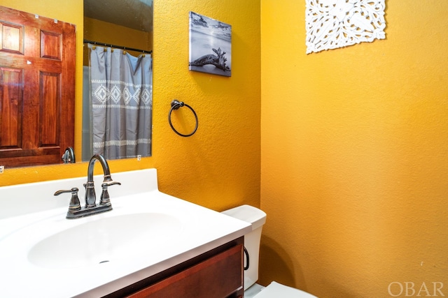 full bath with toilet, a textured wall, and vanity