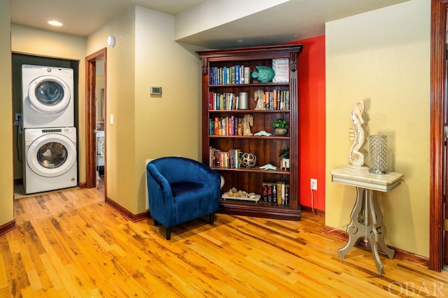 living area featuring light wood-type flooring, stacked washer / dryer, and baseboards