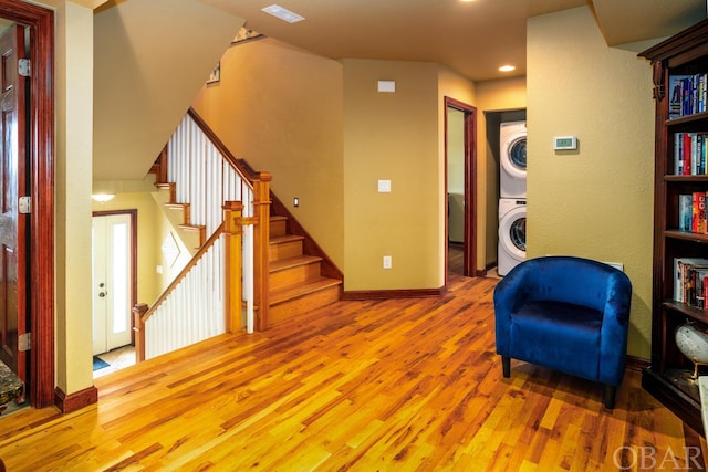 sitting room featuring visible vents, baseboards, stacked washer / drying machine, stairway, and light wood finished floors