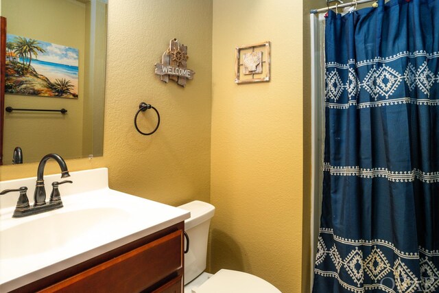 bathroom with toilet, a textured wall, a shower with curtain, and vanity