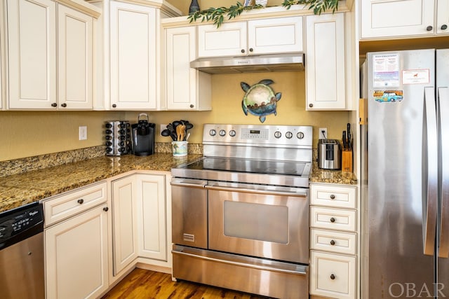 kitchen with appliances with stainless steel finishes, dark stone counters, dark wood-style flooring, and under cabinet range hood