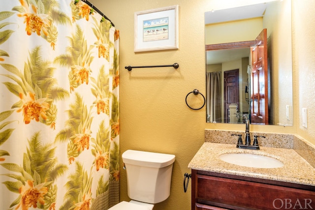 full bathroom with a textured wall, vanity, and toilet