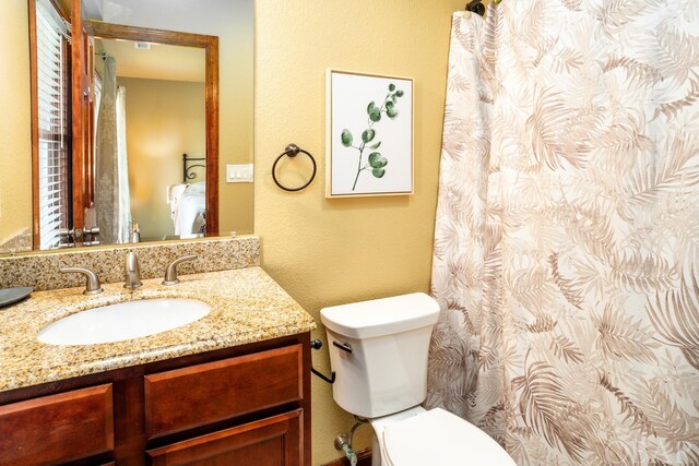 full bathroom with toilet, a textured wall, and vanity