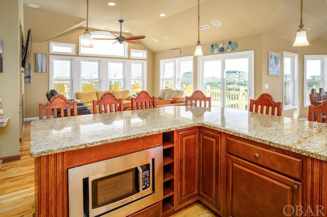 kitchen with lofted ceiling, stainless steel microwave, decorative light fixtures, and light stone countertops