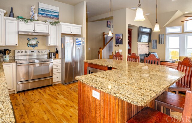 kitchen featuring a center island, decorative light fixtures, stainless steel appliances, under cabinet range hood, and a kitchen bar