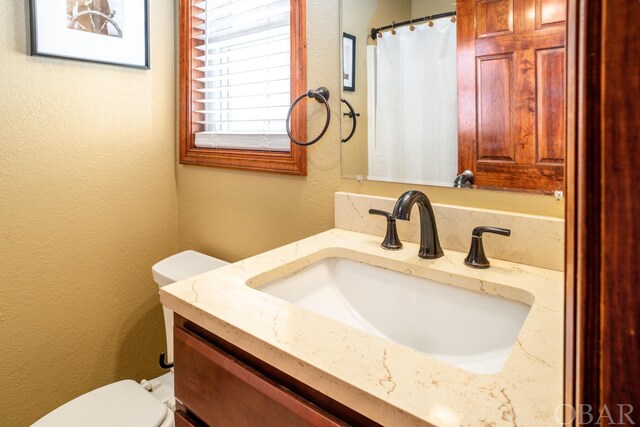 full bathroom with toilet, a textured wall, and vanity