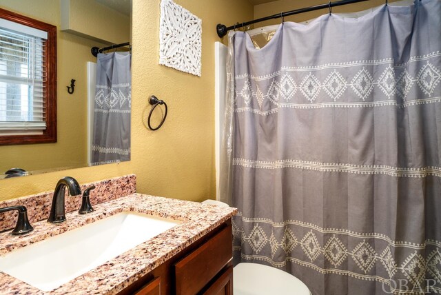 full bathroom featuring toilet, a textured wall, and vanity