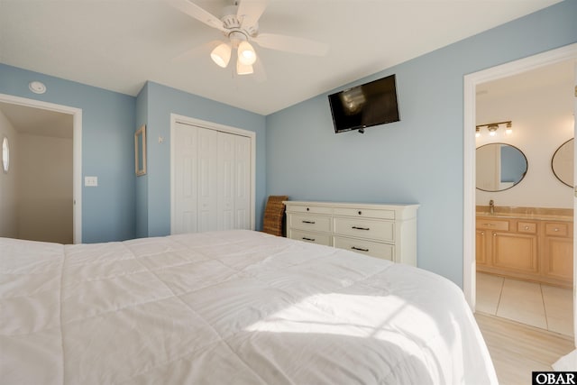 bedroom featuring ensuite bathroom, a sink, a ceiling fan, light wood-style floors, and a closet