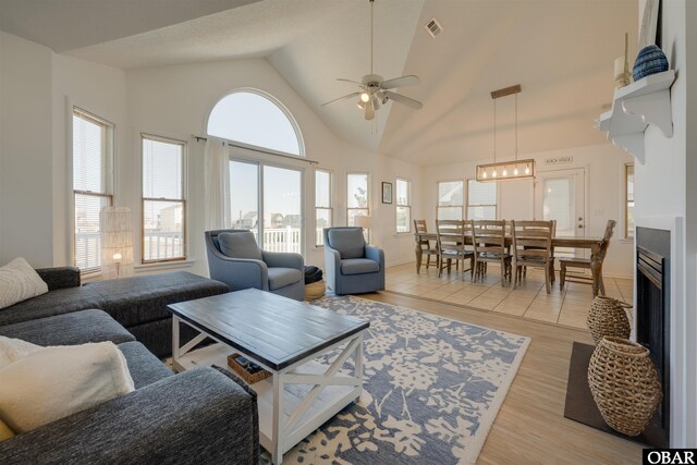 living room with high vaulted ceiling, a wealth of natural light, visible vents, and light wood finished floors