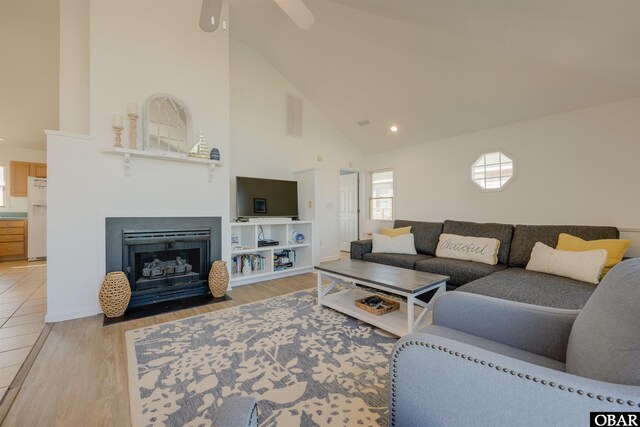 living room featuring light wood-style floors, a fireplace with flush hearth, visible vents, and high vaulted ceiling