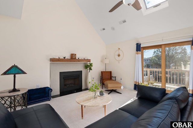 living room featuring high vaulted ceiling, a skylight, a fireplace with flush hearth, visible vents, and carpet