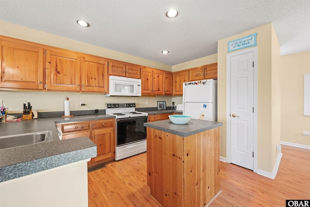 kitchen with dark countertops, white appliances, a kitchen island, and light wood-style floors