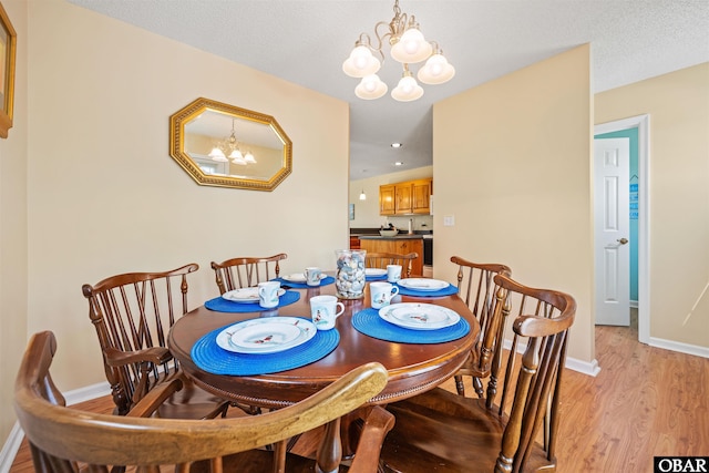 dining space featuring light wood-style floors, a textured ceiling, baseboards, and a notable chandelier