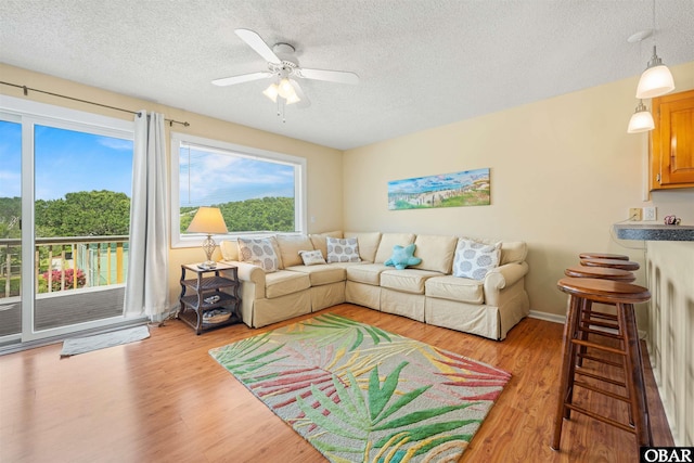 living area with ceiling fan, a textured ceiling, and light wood-style flooring