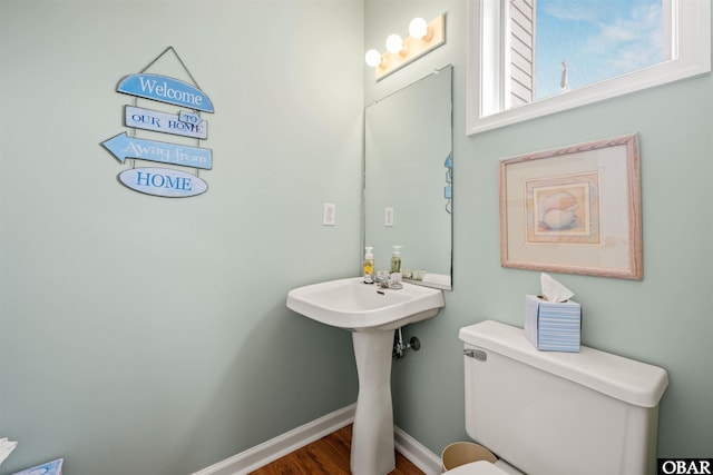 half bath with a sink, toilet, baseboards, and wood finished floors