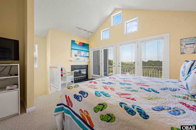 bedroom featuring rail lighting, a glass covered fireplace, carpet flooring, high vaulted ceiling, and access to outside