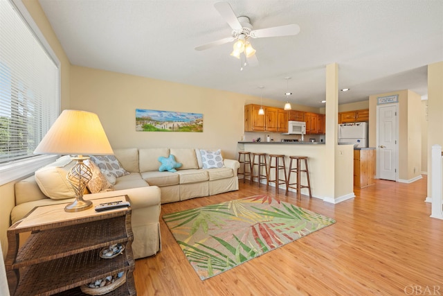 living area with ceiling fan, light wood-style flooring, and baseboards