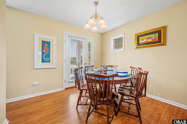 dining area featuring baseboards, a notable chandelier, a textured ceiling, and light wood finished floors