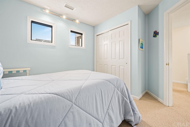 bedroom featuring a textured ceiling, light carpet, visible vents, baseboards, and a closet