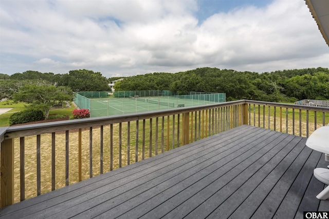 wooden terrace featuring a tennis court, fence, and a yard