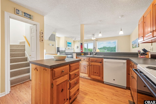 kitchen with a center island, dark countertops, light wood-style flooring, white dishwasher, and a sink