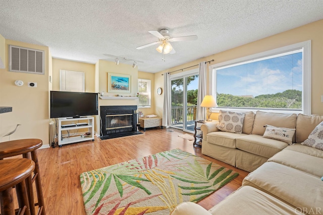 living room with a healthy amount of sunlight, a fireplace with flush hearth, visible vents, and wood finished floors