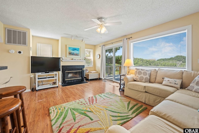 living room featuring track lighting, ceiling fan, wood finished floors, and visible vents
