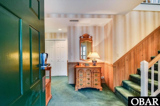 carpeted foyer entrance featuring a wainscoted wall, wooden walls, stairs, and visible vents